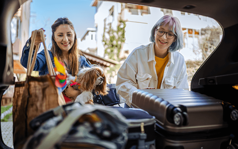 women smiling and packing luggage into car
